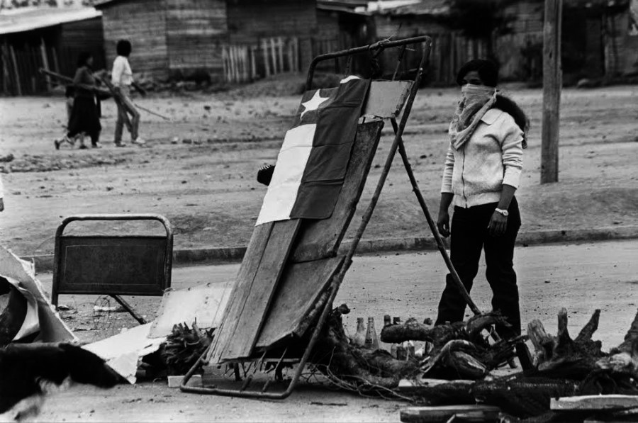 Kena Lorenzini, mujer encapuchada levanta una barricada en una toma de terreno en la comuna de Puente Alto, Santiago, Chile, fotografía análoga, 1984. Cortesía de la artista.