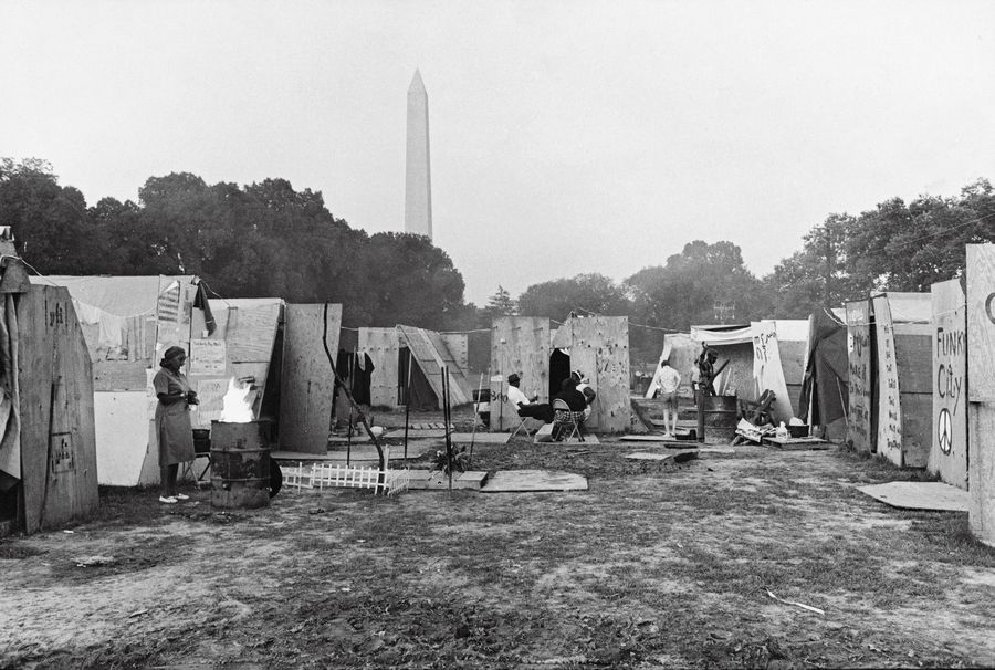 Jill Freedman, Resurrection City. Residents outside their shelters relax in the shadow of the Washington Monument in Resurrection City, a three thousand person tent city on the Washington Mall as part of the Poor People’s Campaign. 1968. The Jill Freedman Irrevocable Trust.