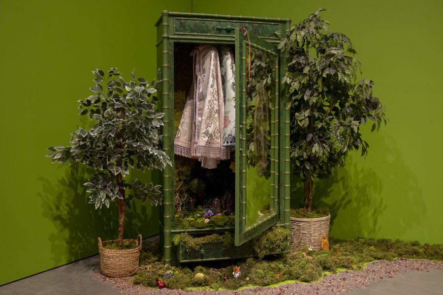 un armario de color verde con prendas de vestir adentro rodeado de plantas es un altar de la artista chicana Amalia Mesa-Bains
