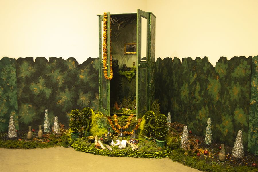 un altar hecho con un armario y musgo celebra las tradiciones de la cultura chicana. es de color verde y está en el centro de una sala de un museo